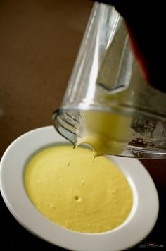 a person pouring liquid into a white bowl filled with yellow liquid from a blender