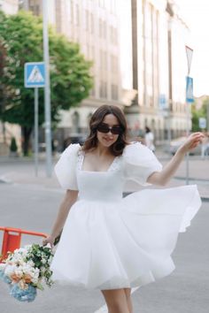 a woman in a short white dress is walking down the street with her arms outstretched