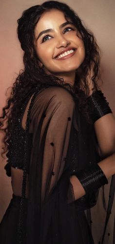 a woman with curly hair wearing a sheer black top and holding her arm around her neck