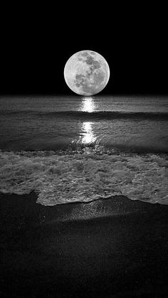 the full moon is shining over the ocean and waves on the beach in black and white