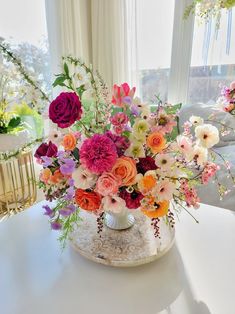 a vase filled with lots of colorful flowers on top of a table next to a window