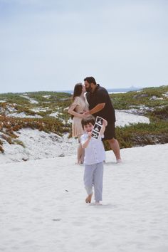 a man, woman and child standing in the sand