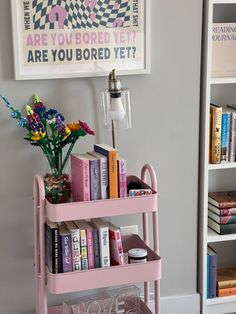 a pink cart with books and flowers on it in front of a book shelf filled with books