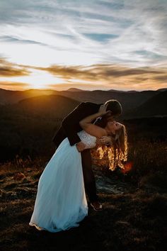 a bride and groom kissing on top of a mountain at sunset with the sun setting behind them