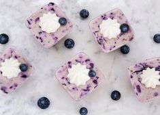 four blueberry cheesecakes with whipped cream and blueberries around them on a marble surface