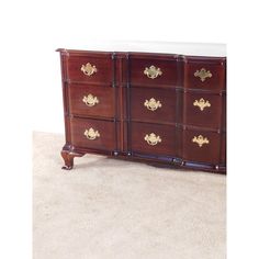 a wooden dresser with many drawers and gold hardware on it's doors, sitting on carpeted flooring