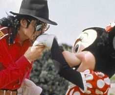 a man in a mickey mouse costume is kissing another person's face with one hand