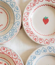 four plates with hearts and a strawberry painted on the side, all in different colors