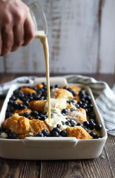 someone pouring dressing into a casserole dish with blueberries and biscuits