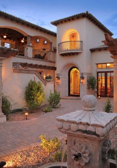 a large house with a fountain in front of it at dusk or dawn, as seen from the driveway