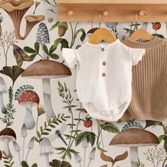 a baby's bodysuit hanging on a wall with mushrooms and leaves