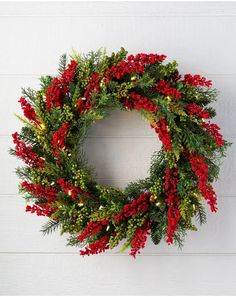 a christmas wreath hanging on the side of a white wall with red berries and greenery