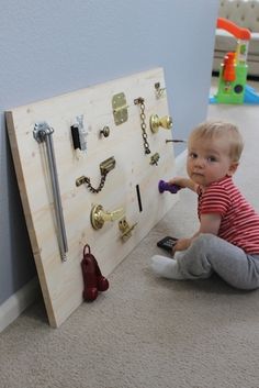 a baby sitting on the floor next to a wooden peg board with hooks and keys