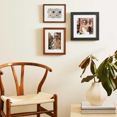 a wooden chair sitting next to a white vase filled with flowers and pictures on the wall