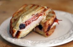 a sandwich cut in half on a white plate with syrup and fruit filling the side