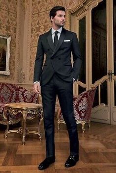 a man in a black suit and tie standing on a wooden floor next to chairs