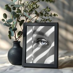 a black vase with a plant next to it and a framed photograph of a woman's eye