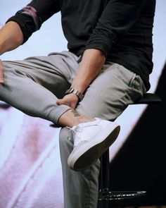 a man sitting on top of a chair with his legs crossed and wearing white sneakers