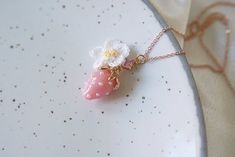 a strawberry necklace with a flower on it sitting on a white plate next to a gold chain