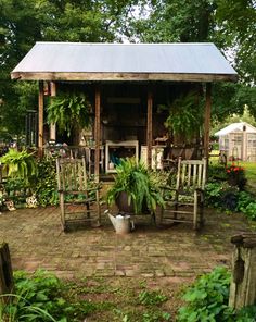 a garden shed with chairs and potted plants on the patio, surrounded by greenery