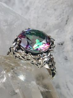 Rainbow Mystic Topaz (Simulated or Natural) Ring Speechless Design#103 MADE TO ORDER Inspired by Victorian era filigree designs, I now offer this stunning Antique inspired ring in sterling silver. This fabulous ring is set with a 6ct (Simulated or Natural, choose option above) Mystic Topaz gemstone. The round full cut high-quality rainbow gemstone is 12mm (just shy of 1/2th of an inch) in diameter. The inside of the band is marked 925 for sterling. Notice the beautiful intricate bow and floral-l Branch Engagement Ring, Raw Opal Ring, Antique Style Rings, Rainbow Topaz, Sapphire Solitaire Ring, Turquoise Gold Ring, Mystic Topaz Ring, Blue Topaz Jewelry, Victorian Ring