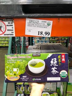 a person holding up a box of green tea in front of a shelf with other items