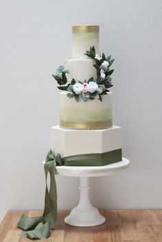 a three tiered wedding cake sitting on top of a wooden table next to a green ribbon