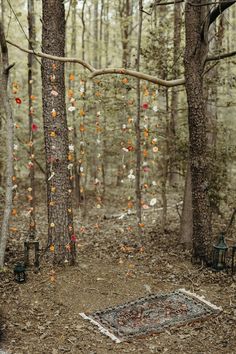 an outdoor ceremony in the woods with orange and white decorations hanging from trees, lanterns and rugs