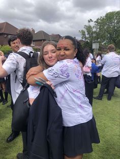 two young women hugging each other in front of some people on the grass with their arms around one another