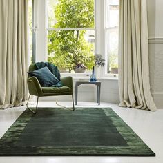 a green chair sitting in front of a window next to a rug on the floor