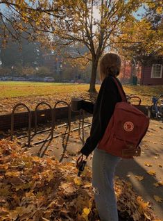 a woman with a red backpack is walking down the street in fall leaves and trees