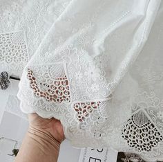 the white lace is being held up by someone's hand on top of a piece of fabric