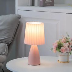 a white table with a lamp on it next to a flower pot and a chair