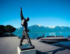 there is a statue of a man that is on the dock next to water and mountains