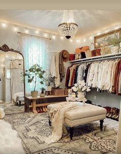 a bedroom with a bed, ottoman and closet full of clothes on hangers next to a chandelier