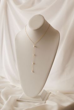 a white mannequin with a gold necklace on it's neck, sitting on a white cloth