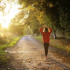 a woman walking down a dirt road with her hands on her head and trees in the background