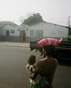 a woman carrying a child on her back across the street from a truck that is parked in front of a building