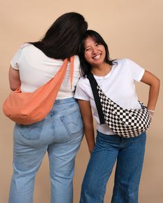 two women standing next to each other with their backs turned and one holding a checkered purse