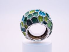 A gorgeous enameled ring in a size 7 1/2. Featuring a beautiful selection of blue and green enamel colors with a lovely emerald hidden on the back of the ring for the wearer to admire. This sculptural ring wears very comfortably and will bring a splash of bright color and joy to any day; sure to pair well with any outfit. Materials: Glass Enamel, Natural Emerald, Sterling Silver Enamel Fine Jewelry, Elegant Green Enamel Ring, Unique Green Open Ring Jewelry, Modern Green Enamel Jewelry, Green Enamel Round Ring, Unique Green Ring Jewelry, Green Enamel Rings As A Gift, Modern Green Round Dome Ring, Unique Hand Painted Enamel Rings