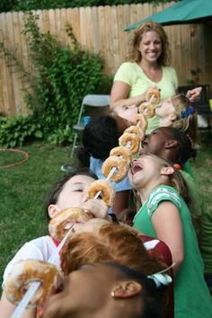 a group of children and adults eating donuts in the back yard with an adult