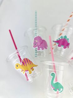 plastic cups filled with different types of drinking straws and paper dinosaurs on them, sitting on a white surface