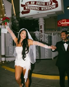 a bride and groom walking down the street in front of a wedding venue at night