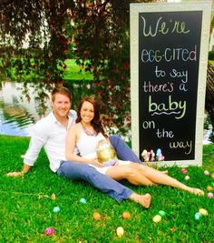 a man and woman sitting on the grass with an egg in front of a sign that says we're egg - tired to say there's a baby on the way