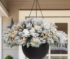 a hanging planter filled with white flowers and pine cones on the front door porch