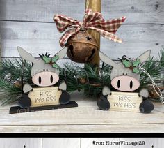 two little pigs are sitting next to each other on a mantel with pine branches