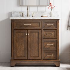 a bathroom vanity with marble top and wooden cabinetry, along with a gold framed mirror on the wall