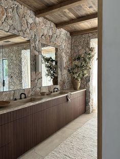 a stone bathroom with two sinks and large mirrors on the wall next to each other