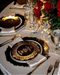 the table is set with black and gold plates, silverware, and red roses