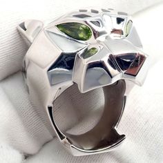 The Cartier Panther 'Panthere' ring is a stunning piece of luxury jewelry, embodying the brand's iconic design. Forged in 18k white gold, this large ring features a panther head that showcases vibrant peridot stones as eyes, set against a backdrop of black onyx and white gold. The panther's features are further highlighted by intricate lacquer detailing, adding depth and texture to the design. The juxtaposition of the peridot’s bright green against the dark onyx creates a striking visual contras Cartier Luxury Gemstone Jewelry, Luxury Cartier Gemstone Jewelry, Elegant Cartier Jewelry, Cartier Gemstone Jewelry For Gifts, Fine Jewelry Platinum Emerald Ring With Polished Finish, Platinum Emerald Ring With Polished Finish, Modern Platinum Gemstone Rings, Modernist White Gold Diamond Jewelry, Luxury Polished Emerald Ring